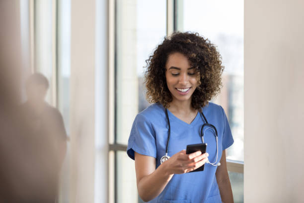 glad sjuksköterska kontrollerar meddelanden på smartphone medan i sjukhus hall - happy scrubs nurse phone bildbanksfoton och bilder