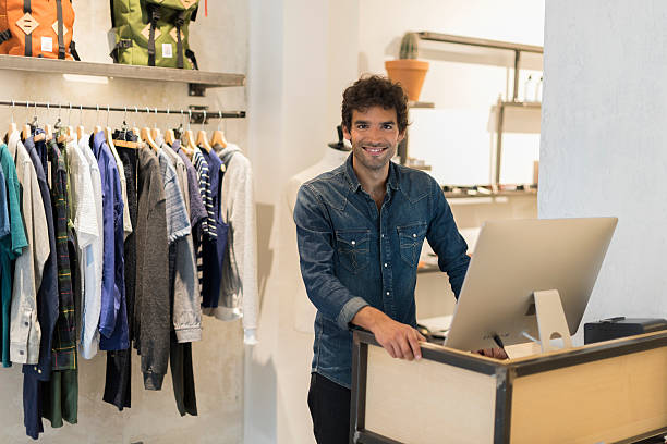 Cheerful seller man in clothing store. Working on computer stock photo