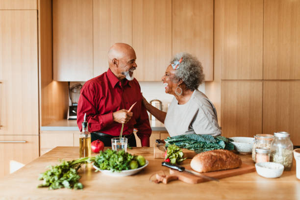 fröhliches seniorenpaar bereitet veganes essen in der küche zu - oma kocht stock-fotos und bilder