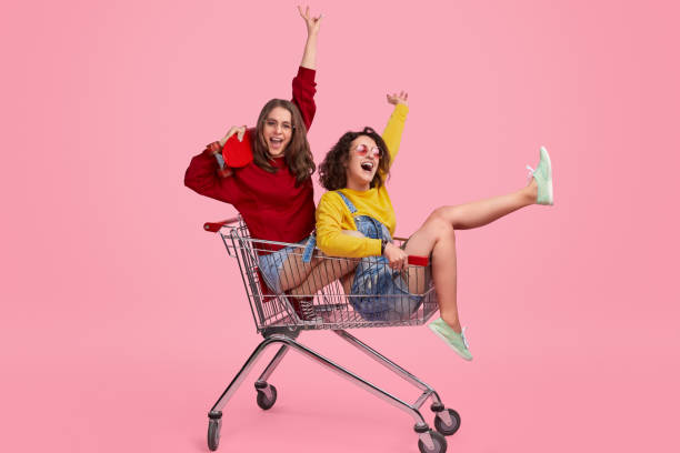 cheerful sisters riding shopping trolley - friends color background imagens e fotografias de stock