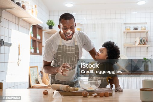 istock Cheerful smiling Black son enjoying playing with his father while doing bakery at home. Playful African family having fun cooking baking cake or cookies in kitchen together. 1311089680
