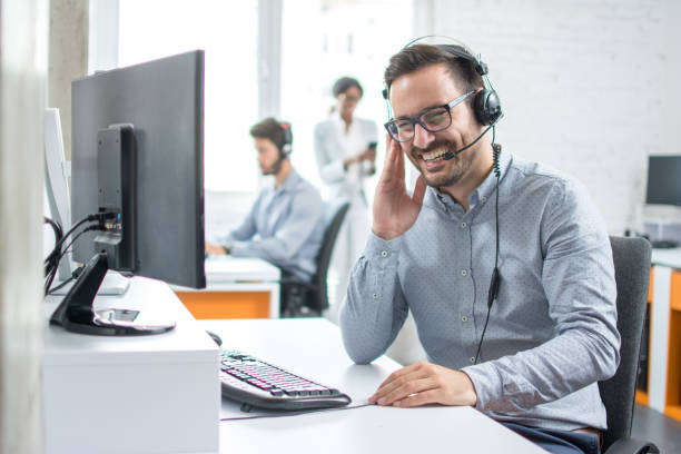 Cheerful technical support dispatcher talking with customer using headset in call center stock photo