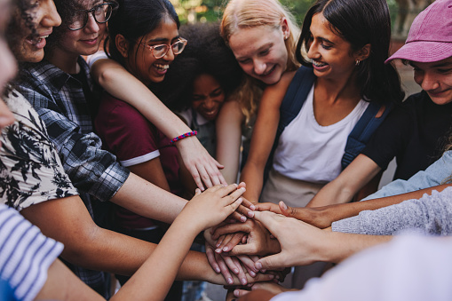 Diverse teenagers smiling cheerfully while putting their hands together in a huddle. Group of generation z youngsters symbolizing team spirit and togetherness.