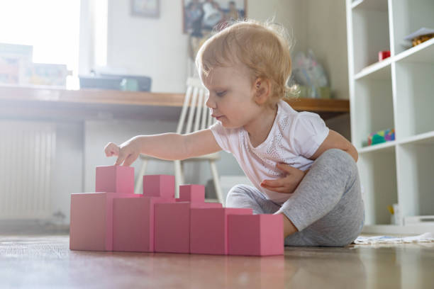 Cheerful toddler arrangement pink cubes assembling tower educational Maria Montessori materials stock photo