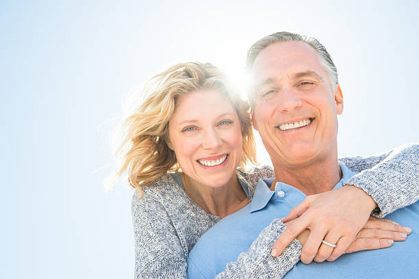 Cheerful Woman Embracing Man From Behind Against Sky stock photo
