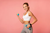 Strength And Cardio Workout. Smiling Woman Exercising With Dumbbells Over Pink Background In Studio. Free Space