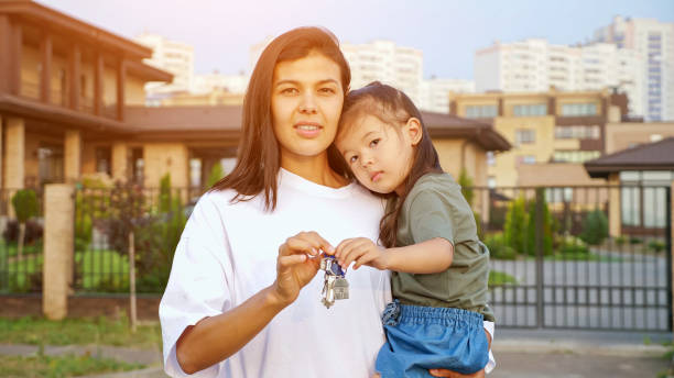 Cheerful woman shows keys of apartment holding daughter stock photo