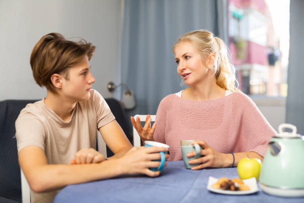 Cheerful woman talking friendly with teenage son during breakfast stock photo