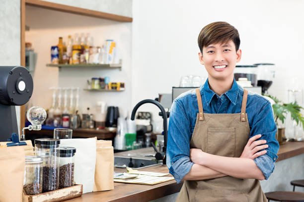 Cheerful young Asian man entrepreneur in coffee shop Cheerful young Asian man entrepreneur standing at counter in his own coffee shop bar drink establishment stock pictures, royalty-free photos & images