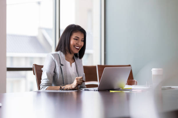 Cheerful young businesswoman video chats with colleague Beautiful young businesswoman smiles as she participates in a video conference with a colleague. She is using a laptop. one young woman only stock pictures, royalty-free photos & images