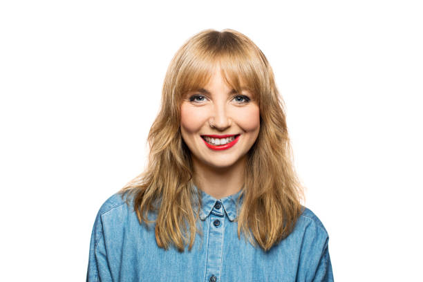 Cheerful young female against white background Portrait of cheerful young woman against white background. Happy female is wearing denim shirt. She is having blond hair. bangs hair stock pictures, royalty-free photos & images