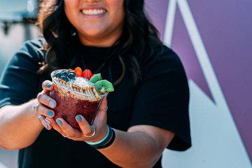 Cheerful Young Latina Woman Holding a Healthy Acai Food Bowl Outside a Food Truck in the Summer on a Sunny Day