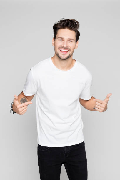 Cheerful young man pointing at himself Portrait of cheerful young man pointing at himself on grey background white t shirt stock pictures, royalty-free photos & images