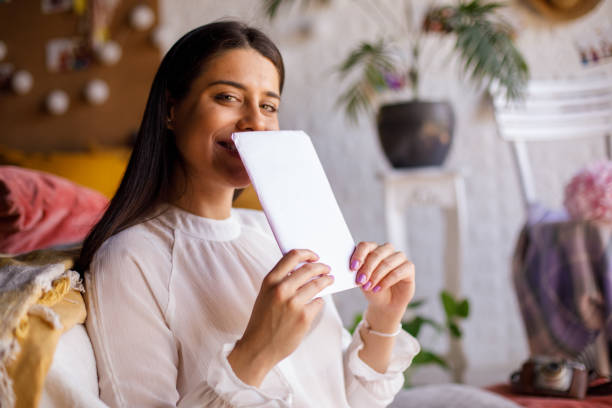 Cheerful young woman hiding her smile behind a love letter from a crush stock photo