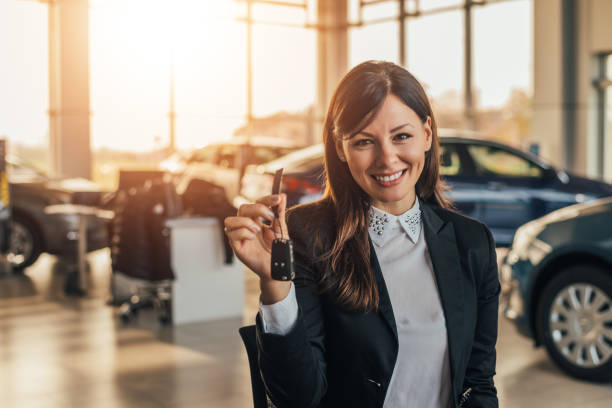 Cheerful young woman showing her new car key at dealership. Cheerful young woman showing her new car key at dealership. car salesperson stock pictures, royalty-free photos & images