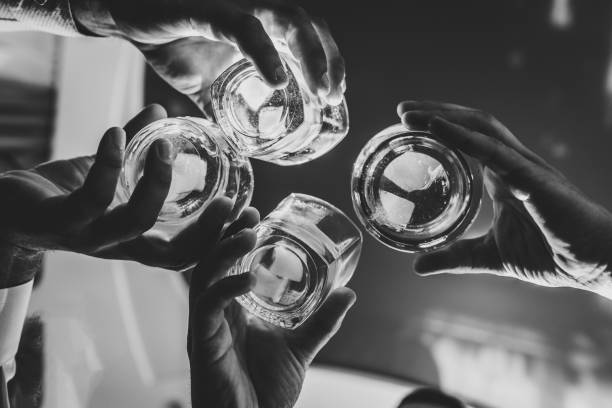 Cheers! Close up of men celebrate and raise glasses of whiskey drink alcoholic beverage in the pub. Clink glasses of rum. Businessmen spending time together drinking brandy. Black and white. stock photo