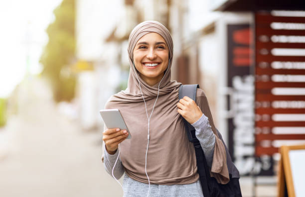 het vrolijke arabische meisje dat door stad loopt en muziek luistert - arabic student stockfoto's en -beelden