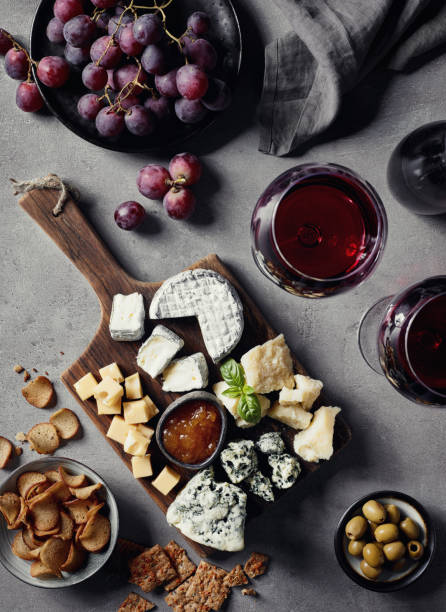 Cheese plate and red wine Cheese plate served with red wine, olives, grapes, jam and bread snacks on gray marble background. Top view. cracker snack photos stock pictures, royalty-free photos & images