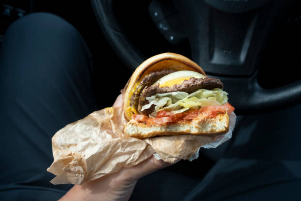 Cheeseburger in Wrapping Papers A person eats a double patty cheeseburger ordered from a drive-through burger chain restaurant in his car. Dangerous forever chemicals, known as PFAS, short for poly and perfluoroalkyl substances, are said to be found in wrappers at major fast food restaurants. burger wrapped in paper stock pictures, royalty-free photos & images
