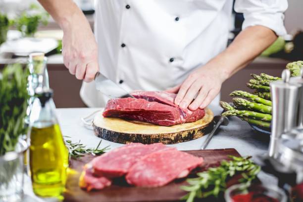 Chef in restaurant kitchen cooking,he is cutting meat or steak stock photo