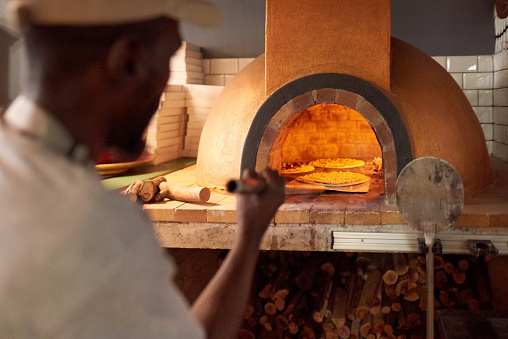 Rear view of a chef taking pizzas out from the oven at a restaurant. Cook baking pizza in an oven.