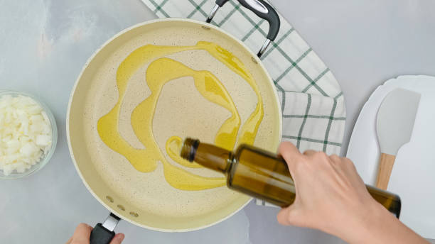 Chef pouring olive oil from bottle into frying pan, close up cooking process, view from above stock photo