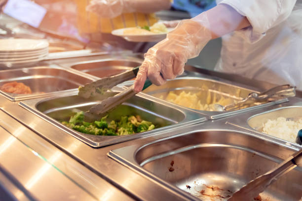 chef-kok staande achter de volledige lunch servicestation met een assortiment van voedsel in trays. - lunchroom stockfoto's en -beelden