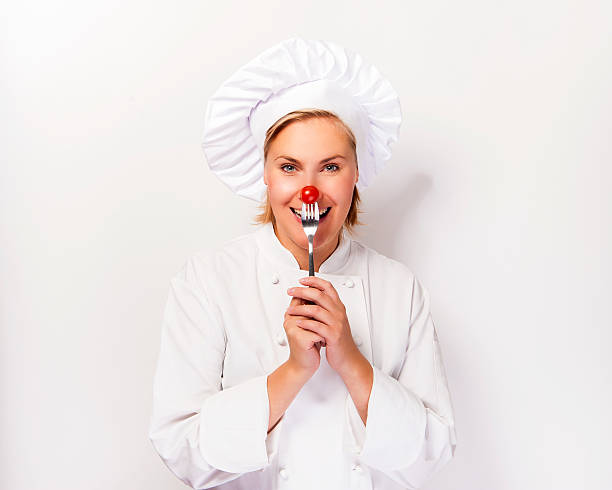 Chef woman holding a fork with tomato against her nose. stock photo