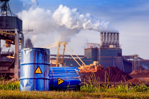 chemical waste drums in front of heavy industry Empty Blue Chemical Waste Drums Lying on an Abandoned Bank with a view on Smoking Exhaust Pipes of a Heavy Industrial Factory water pollution stock pictures, royalty-free photos & images