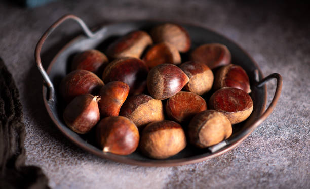 Chestnuts on a artistic metal plate in a rustic dark setup Raw chestnuts on a artistic metal plate in a rustic dark setup chestnut food stock pictures, royalty-free photos & images