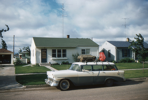1956 Chevrolet station wagon packed for vacation in front of new tract house with TV antenna. Symbols of the affluent post WWII society in USA. Waterloo, Iowa, 1957. Kodachrome scanned film with grain.