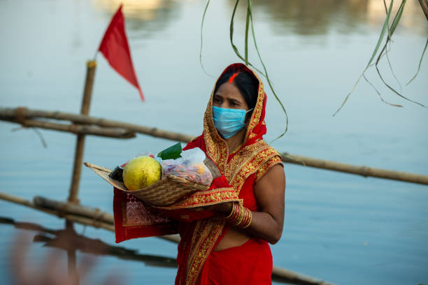 Chhath Pooja An Indian woman in mask performing Hindu ritual during "Chhath Pooja" to worship sun god at the banks of river Yamuna. chhath stock pictures, royalty-free photos & images