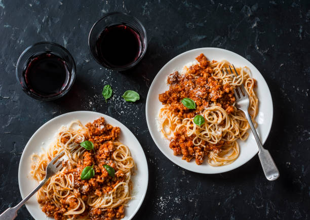 Chicken bolognese spaghetti and glasses of red wine on dark background, top view. Delicious lunch in a mediterranean style, top view. Flat lay Chicken bolognese spaghetti and glasses of red wine on dark background, top view. Delicious lunch in a mediterranean style, top view. Flat lay bolognese sauce stock pictures, royalty-free photos & images
