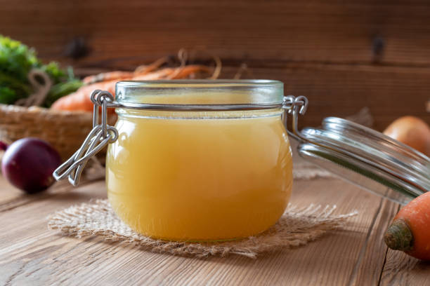 Chicken bone broth in a glass jar and fresh vegetables stock photo