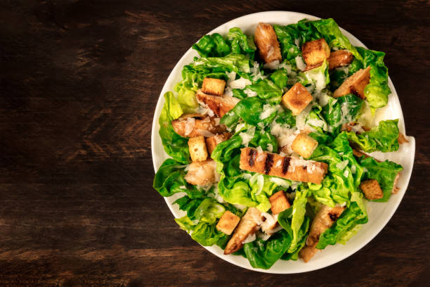 Chicken Caesar salad on rustic background with copyspace An overhead photo of a plate of chicken Caesar salad on a dark rustic background with a place for text chicken salad stock pictures, royalty-free photos & images