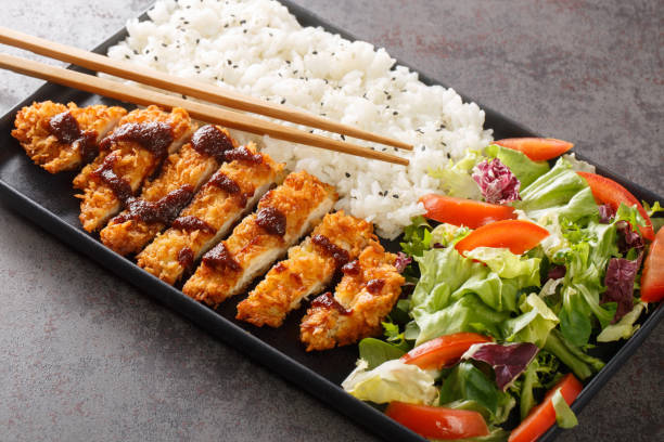 Chicken katsu is a Japanese dish that is also known as panko chicken or tori katsu served with rice and vegetables salad. Horizontal stock photo