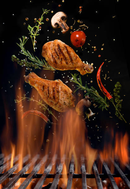 Chicken legs and spicy ingredients flying above flaming red barbeque grill stock photo