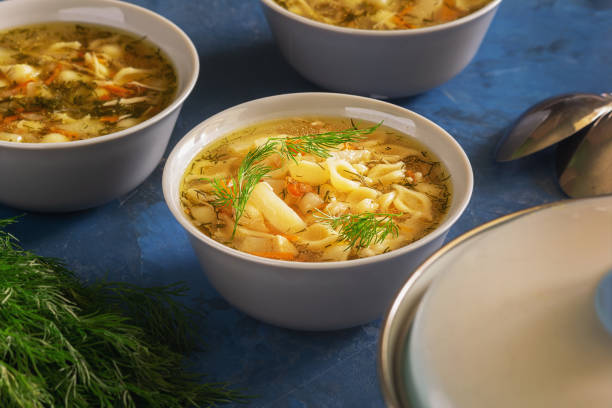 Chicken Noodle Soup with Vegetables Fresh Dinner. Homemade Healthy Meal Served in White Bowl. Poultry Broth with Traditional Pasta Closeup View. Branch of Dill on Table. Nutritious Lunch stock photo