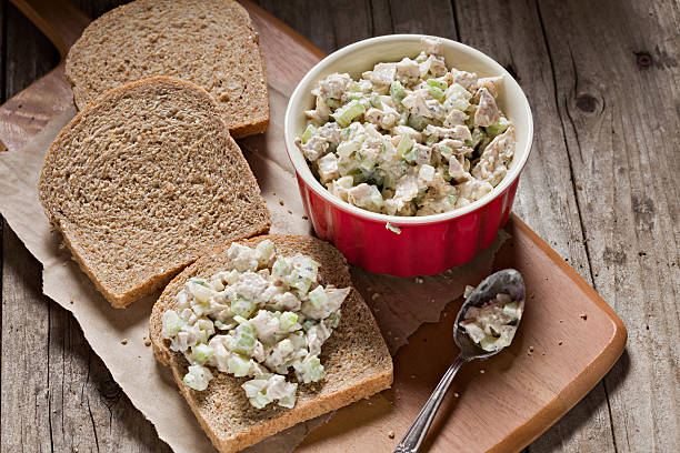 Chicken Salad Sandwich A high angle shot of a red bowl full of chicken salad, several slices of whole grain bread, a spoon and the beginnings of a chicken salad sandwich. Shot on an old rustic wooden picnic table. chicken salad stock pictures, royalty-free photos & images