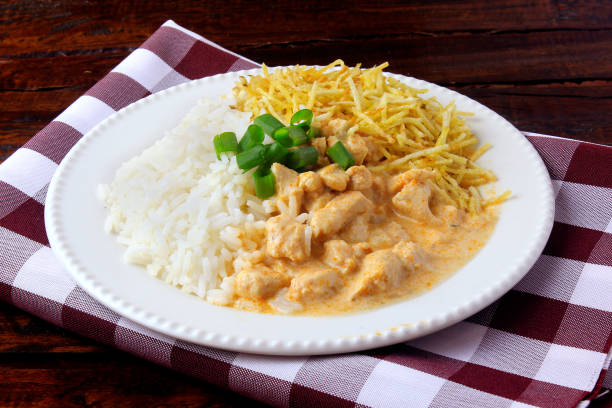 Chicken stroganoff, is a dish originating from Russian cuisine that in Brazil is composed of sour cream with tomato extract, rice and potato chips, on rustic wooden table. stock photo
