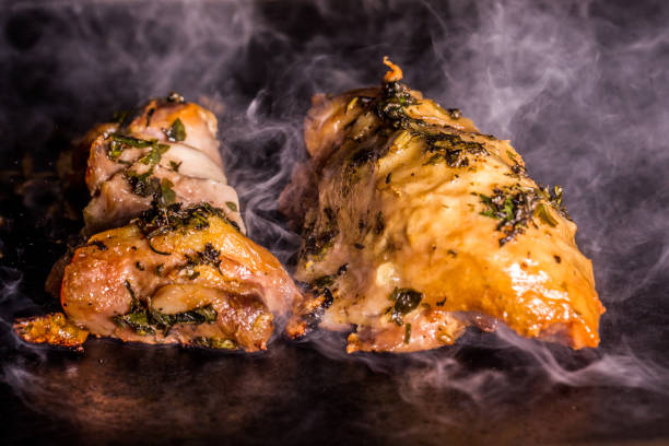 chicken thigh fillet with herbs being grilled on hot plate with smoke on black background. chicken thigh fillet with herbs being grilled on hot plate with smoke on black background. chicken thigh meat stock pictures, royalty-free photos & images