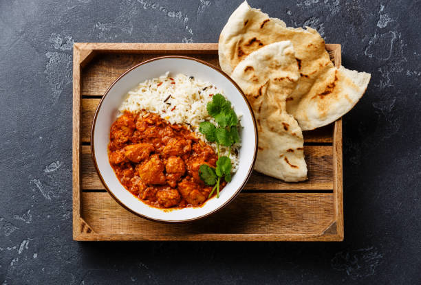 Chicken tikka masala spicy curry meat food with rice Chicken tikka masala spicy curry meat food with rice and fresh naan bread in wooden tray on black stone background naan bread stock pictures, royalty-free photos & images
