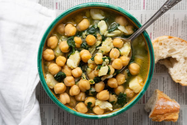 Chickpea stew with spinach and cod Chickpea soup with spinach and dry salted cod in a rustic bowl on a newspaper background chick pea stock pictures, royalty-free photos & images