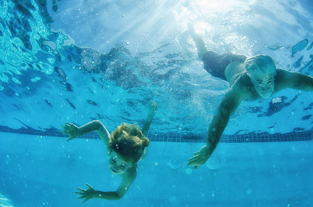 child and grandfather swim down in a pool, underwater photography - retirement overview bildbanksfoton och bilder