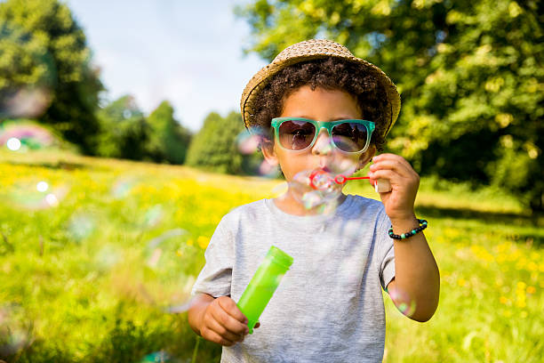 Child blowing bubbles in park Male child blowing bubbles bubble wand stock pictures, royalty-free photos & images