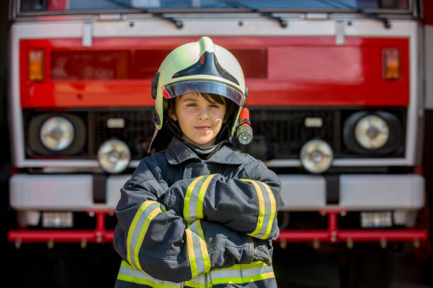 Child, cute boy, dressed in fire fighters cloths in a fire station with fire truck stock photo