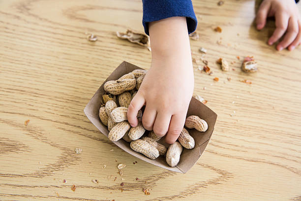 Child eating Peanuts Unrecognizable little boy sits at a table eating peanuts nut food stock pictures, royalty-free photos & images