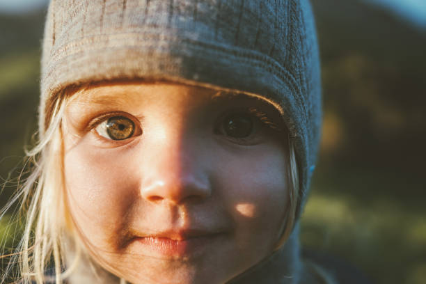 Child face eyes looking at camera cute girl portrait 2 years old toddler outdoor baby smiling wearing hat stock photo