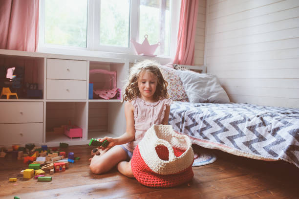 child girl cleaning her room and organize wooden toys into knitted storage bag. Housework and help concept stock photo