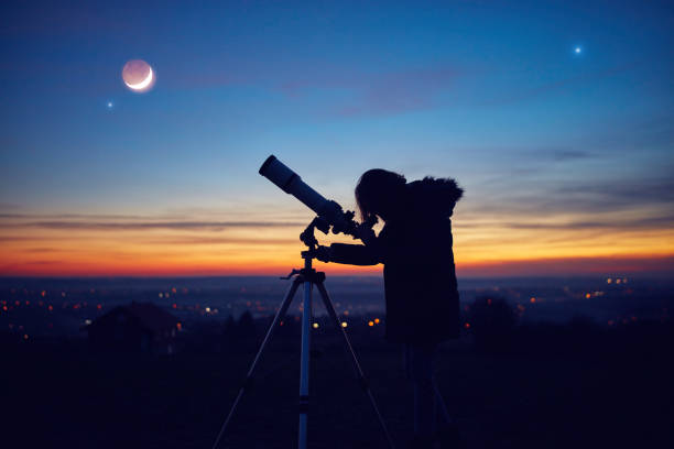 Child girl observing stars, planets, Moon and night sky with astronomical telescope. stock photo